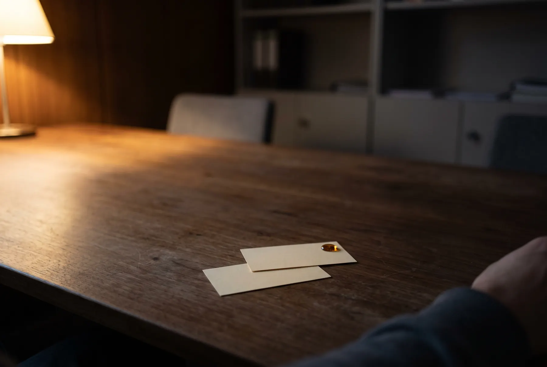 Zwei leere Visitenkarten liegen leicht überlappend auf einem Holztisch, eine Hand zieht sich aus dem Bild zurück.